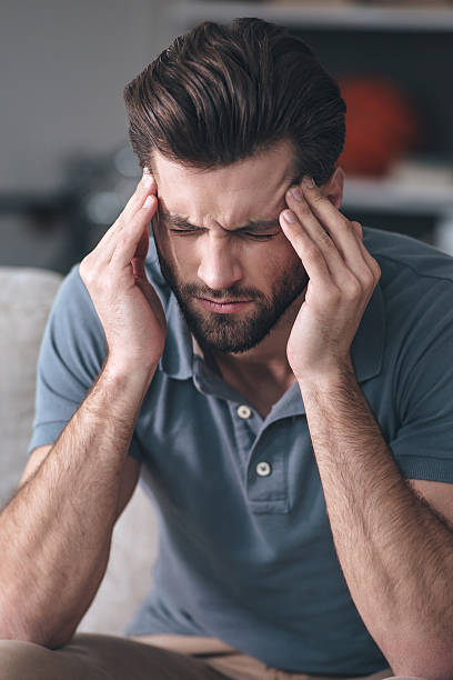 Frustrated  young man touching his head and keeping eyes closedwhile sitting on the couch at home